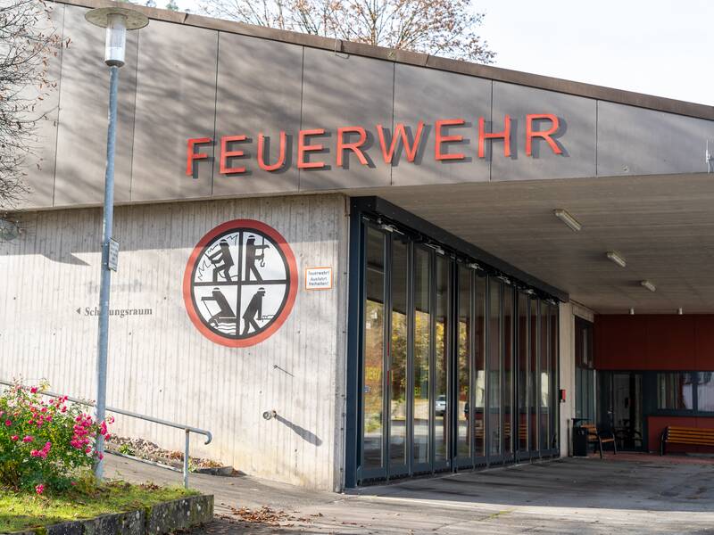 Ein Feuerwehrgebäude mit dem Schriftzug "FEUERWEHR" über dem Eingang und einem runden Symbol an der Wand.